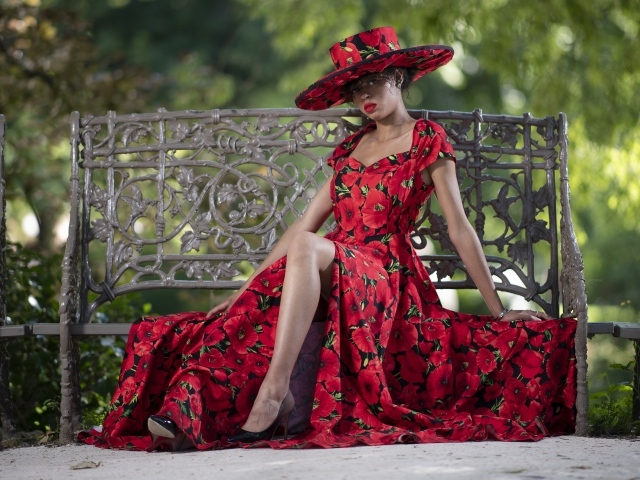 Красивая темнокожая девушка в красном платье сидит на лавке