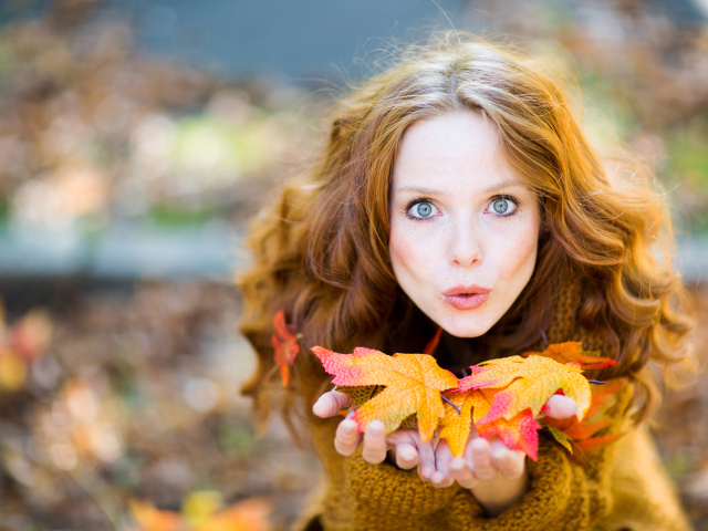 Красивая девушка сдувает листья с ладоней