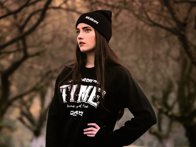 Красивая девушка в черной шапке у деревьев 