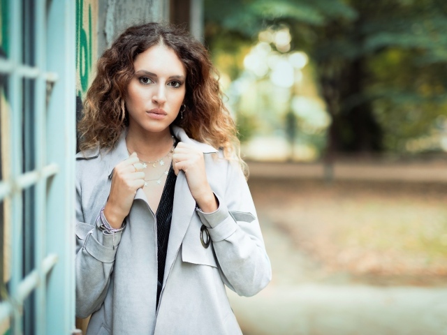 Красивая девушка в сером плаще у стены