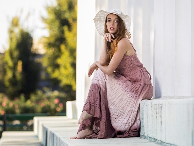 Красивая девушка в белой шляпе сидит на ступеньках 