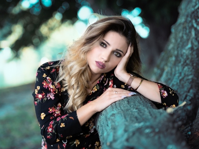 Красивая девушка в цветастом платье у дерева