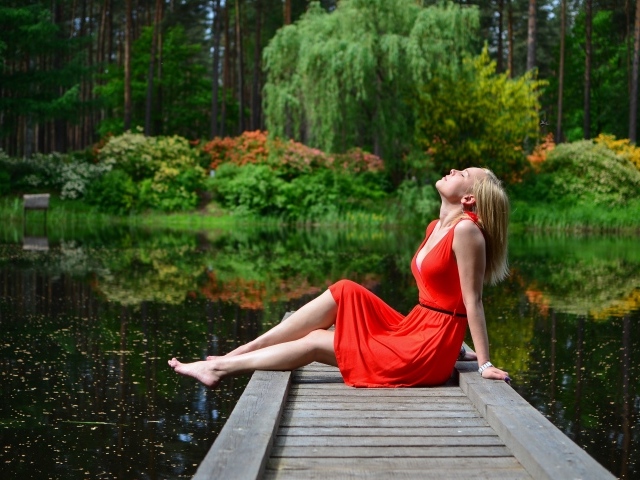 Красивая девушка сидит в красном платье на мосту