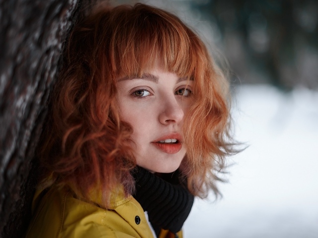 Красивая рыжеволосая девушка стоит у дерева зимой