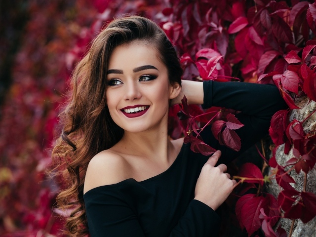 Красивая улыбающаяся длинноволосая девушка у стены с декоративным виноградом