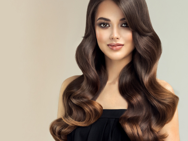 Милая кареглазая девушка с красивыми длинными волосами на сером фоне