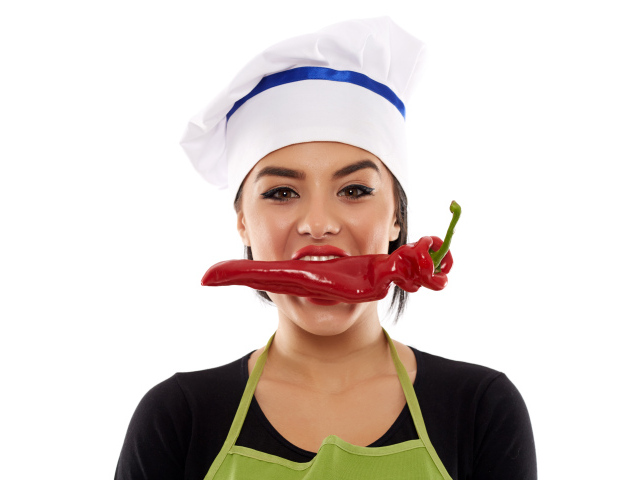 Девушка в шапке повара с красным перцем во рту на белом фоне