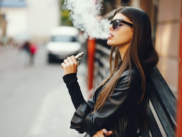 Девушка в солнечных очках пускает дым со рта