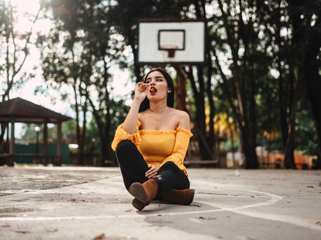 Девушка с леденцом сидит на баскетбольном поле