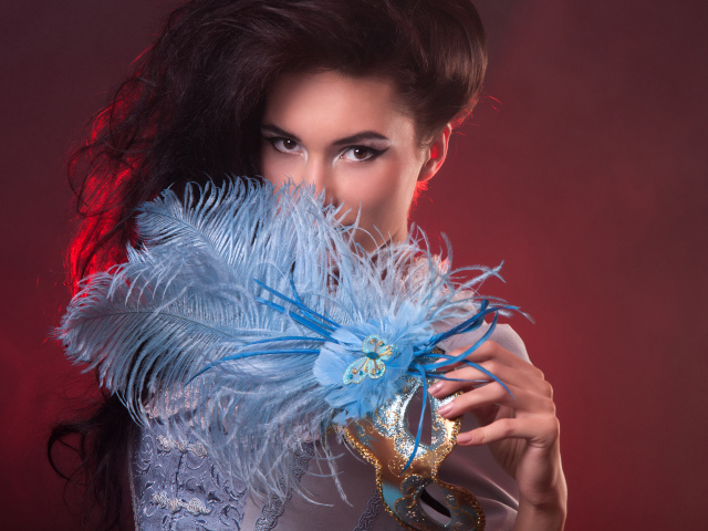 Длинноволосая девушка с маской с перьями в руке