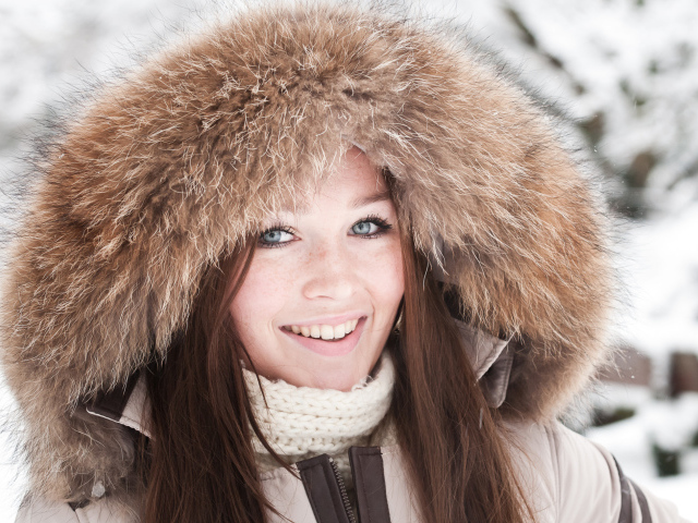 Улыбающаяся голубоглазая девушка в капюшоне зимой