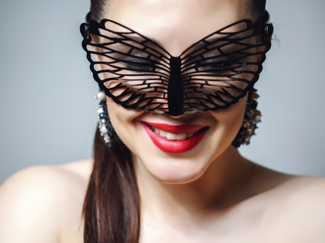 Улыбающаяся девушка в черной маске на сером фоне