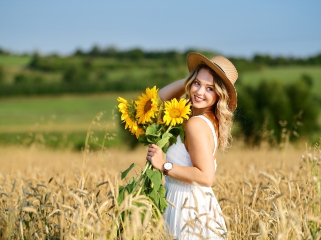 Улыбающаяся девушка на поле с пшеницей с букетом подсолнухов в руке