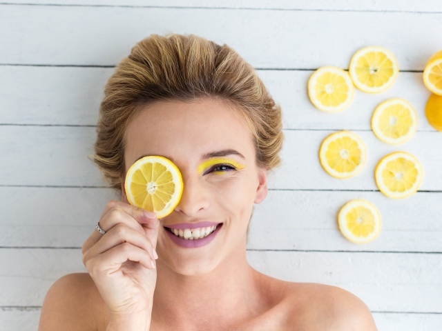 Улыбающаяся девушка приложила лимон к глазу