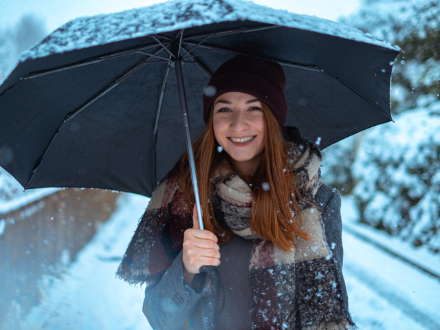 Улыбающаяся молодая девушка под зонтом зимой