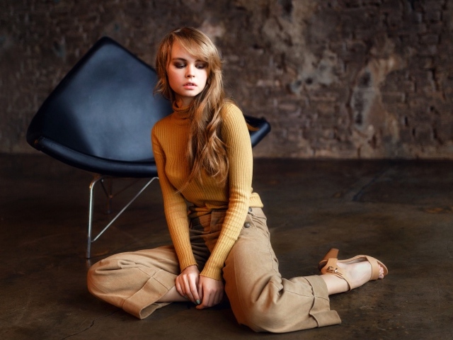 Девушка сидит на полу около черного кресла 