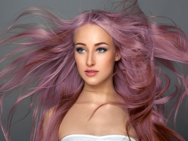 Ветер развивает розовые волосы девушки на сером фоне