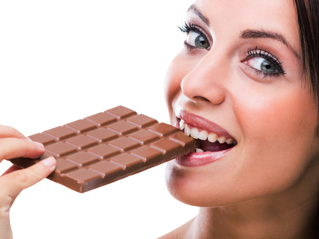 Молодая девушка кусает молочную шоколадку на белом фоне