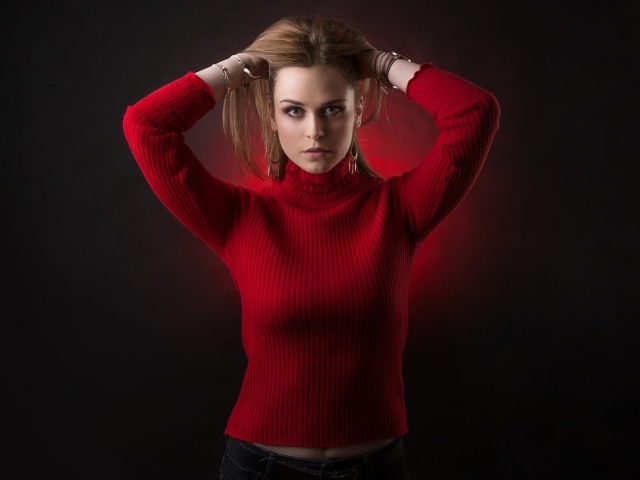 Молодая девушка в красном свитере с руками в волосах