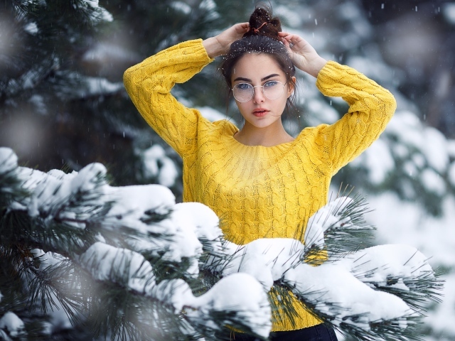 Молодая девушка в очках у заснеженной еловой ветки