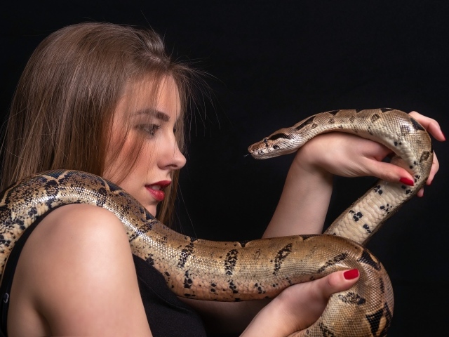 Молодая девушка со змеей в руках на черном фоне