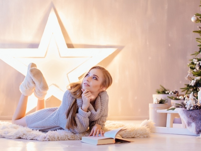 Красивая девушка читает книгу у новогодней елки