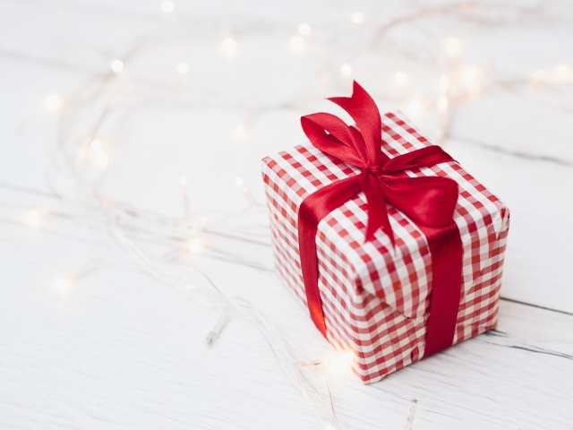 Подарок с красной лентой лежит на столе с гирляндой 