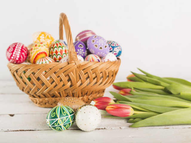Корзина крашеных пасхальных яиц на белом фоне с букетом тюльпанов