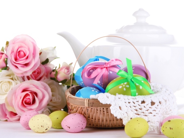 Корзина с пасхальными яйцами на столе с букетом роз и белым чайником