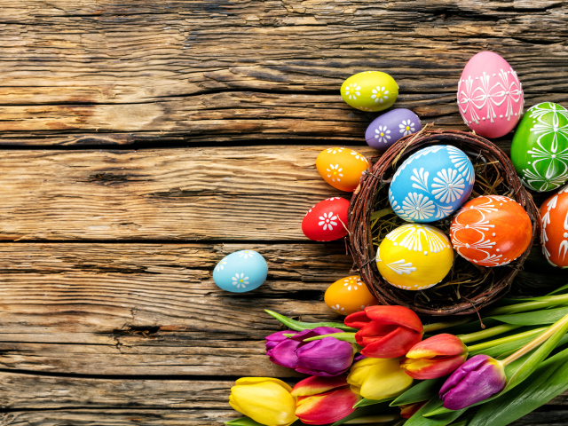 Крашеные пасхальные яйца с букетом тюльпанов на деревянном фоне