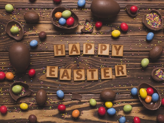Надпись на английском Счастливой Пасхи на столе с шоколадными яйцами и конфетами