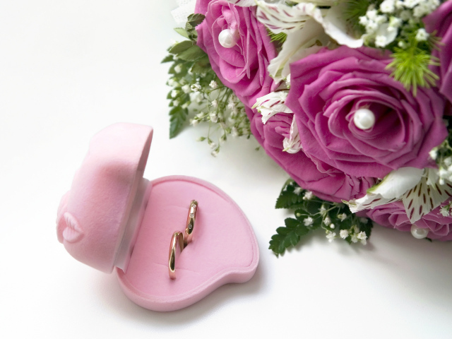 Два обручальных кольца в коробочке на белом фоне с букетом роз
