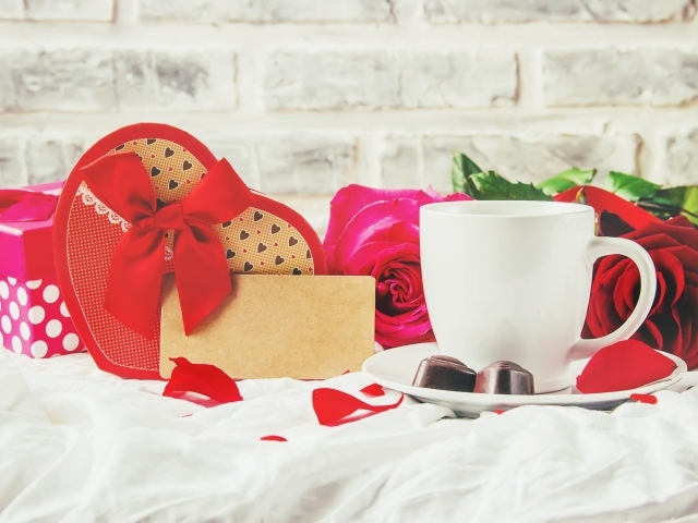 Коробка с подарком на столе с чашкой кофе и красными розами 