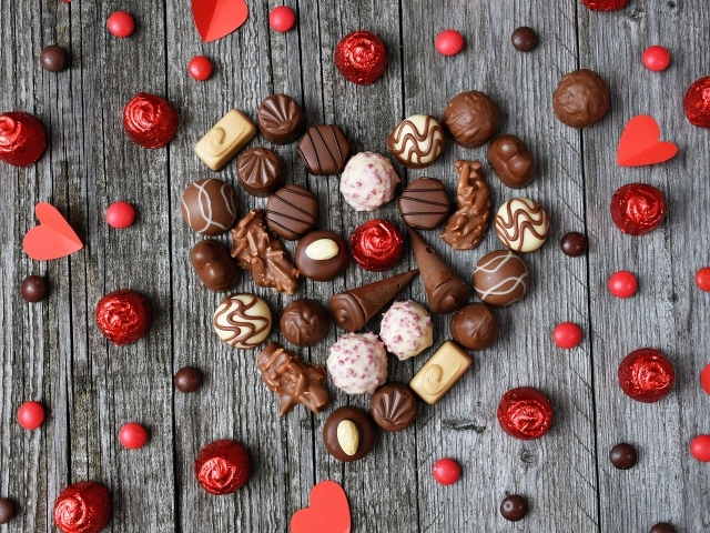 Сердце из шоколадных конфет ассорти на деревянном столе для любимой 
