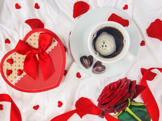 Кружка с кофе и шоколадными конфетами на столе с подарком и красной розой 