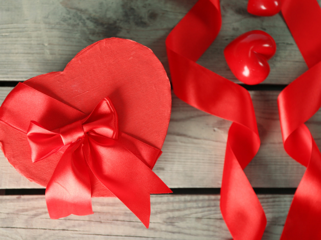 Красная коробка в форме сердца на деревянном столе с красными лентами