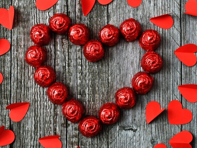 Красное сердце из конфет на деревянном фоне с бумажными сердечками