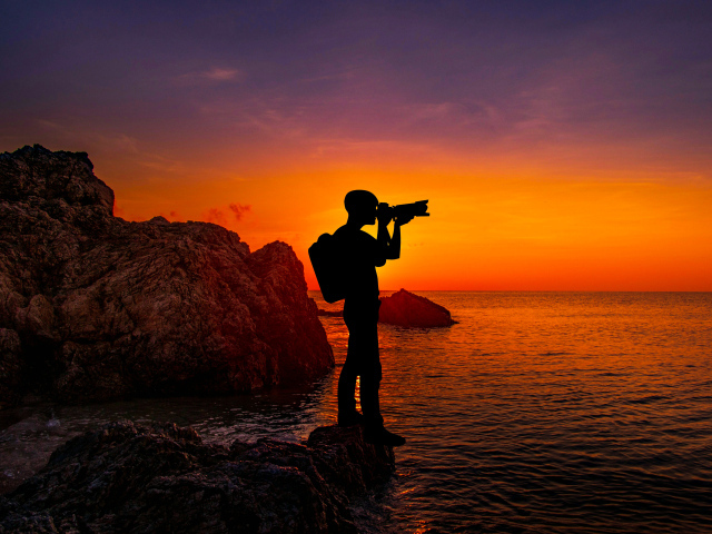 Мужчина фотографирует закат на берегу моря