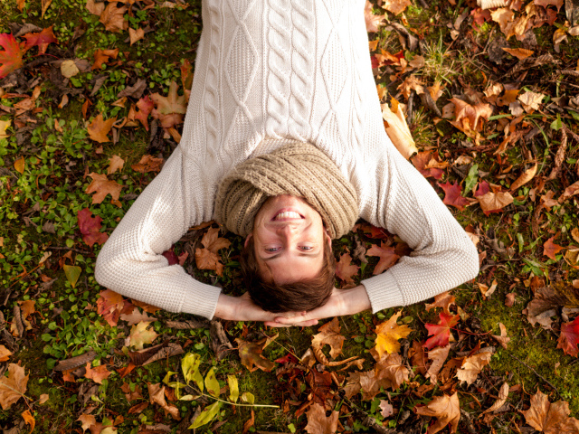 Улыбающийся мужчина в свитере лежит на опавших листьях 