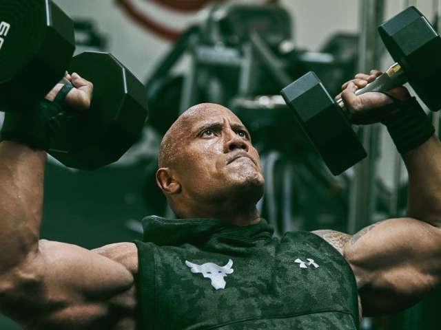 Американский актер, сильный мужчина Дуэйн Джонсон с гантелями в спортзале