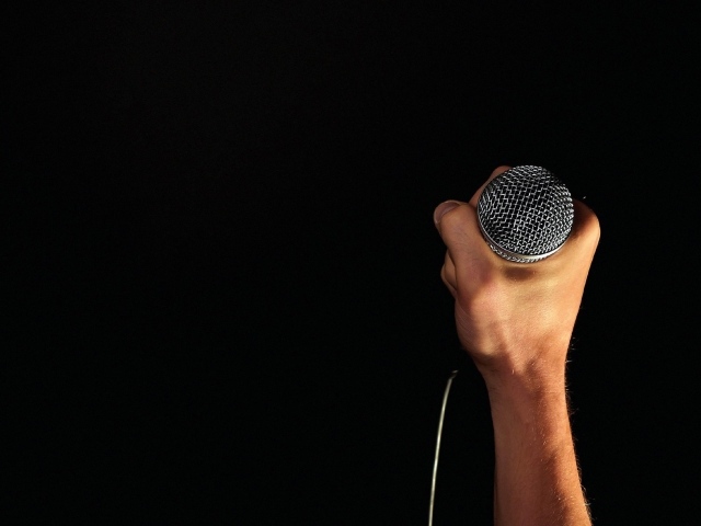 Микрофон в мужской руке на черном фоне