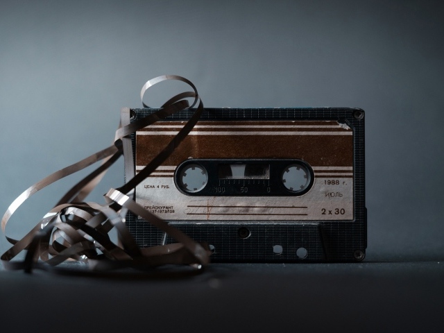 Старая кассета с вытянутой пленкой на сером фоне 