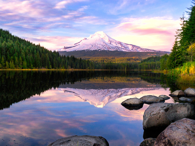 Заснеженная гора отражается в воде озера у зеленого леса