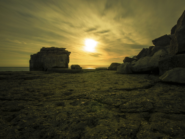 Солнце в облаках освещает камни у моря