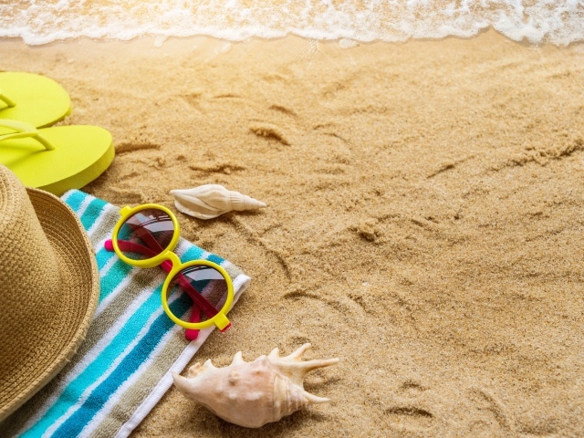 Шляпа, очки, полотенце и ракушки на желтом песке у моря