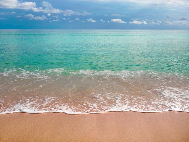 Волны голубого океана на желтом песке под голубым небом