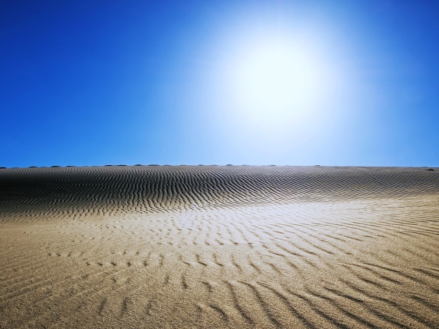 Волнистый песок в пустыне под палящим солнцем в голубом небе 