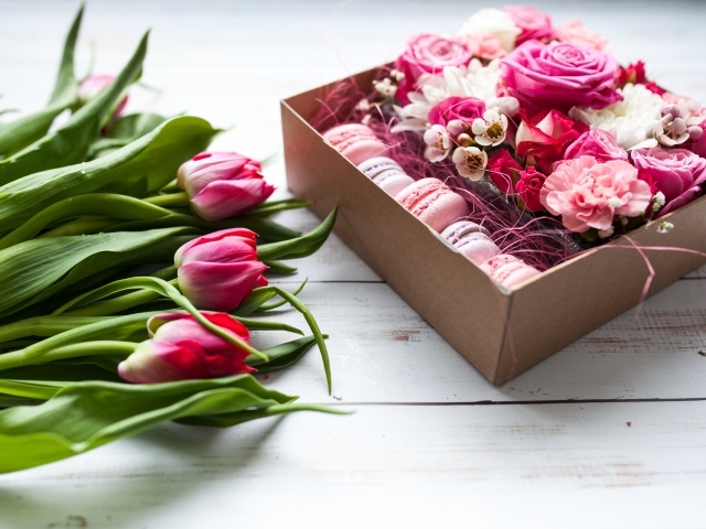 Букет розовых тюльпанов на столе с коробкой печенья макарон и цветами