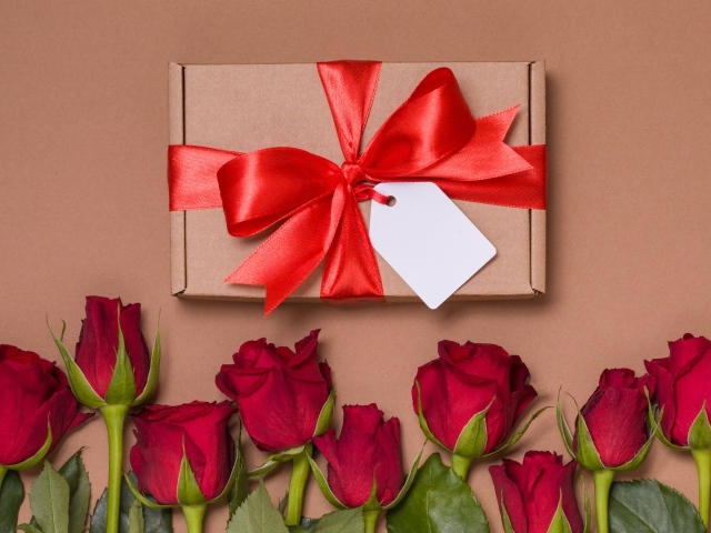 Подарок с красным бантом на бежевом фоне с красными розами