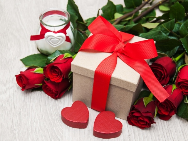 Красивый букет красных роз на столе со свечой и подарком